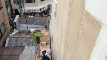 隣の屋根に乗って外壁塗装をする職人